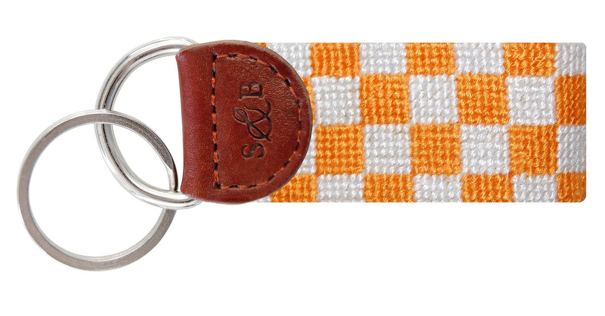 Checkered key fob with orange and white pattern and brown leather accent on a white background