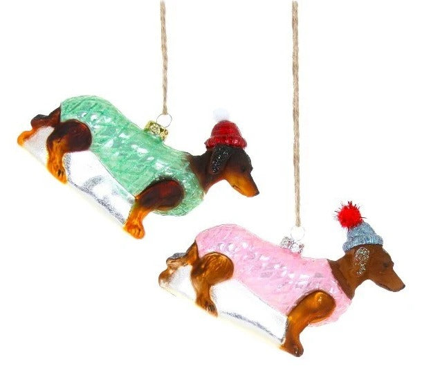 Two glass dog ornaments wearing colorful sweaters hanging on a white background
