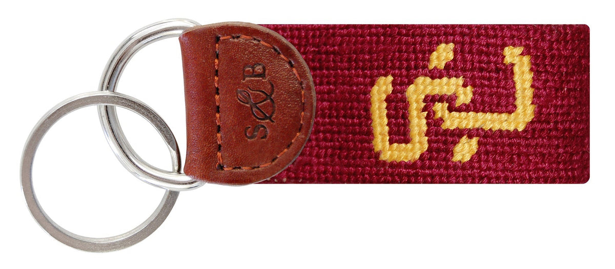 Keychain with red fabric strap and gold text on a white background