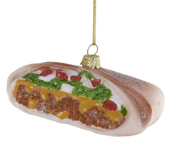 A novelty Christmas ornament shaped like a hot dog filled with cheese, meat, and toppings, hanging from a gold string against a plain white background.