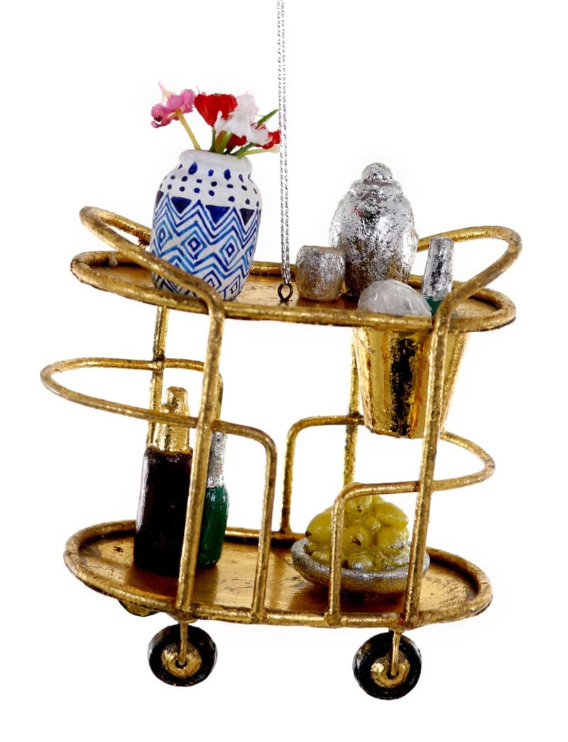 A gold-finished two-tier hanging bar cart with decorative props including a blue and white patterned vase with flowers, a small silver bird figurine, and bottles, shown on a plain white background.