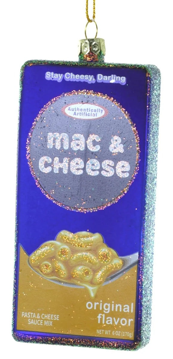 A rectangular Christmas ornament shaped like a box of mac and cheese sauce mix, featuring a purple and gold design with the words 'Stay Cheesy, Darling' and 'mac & cheese'.