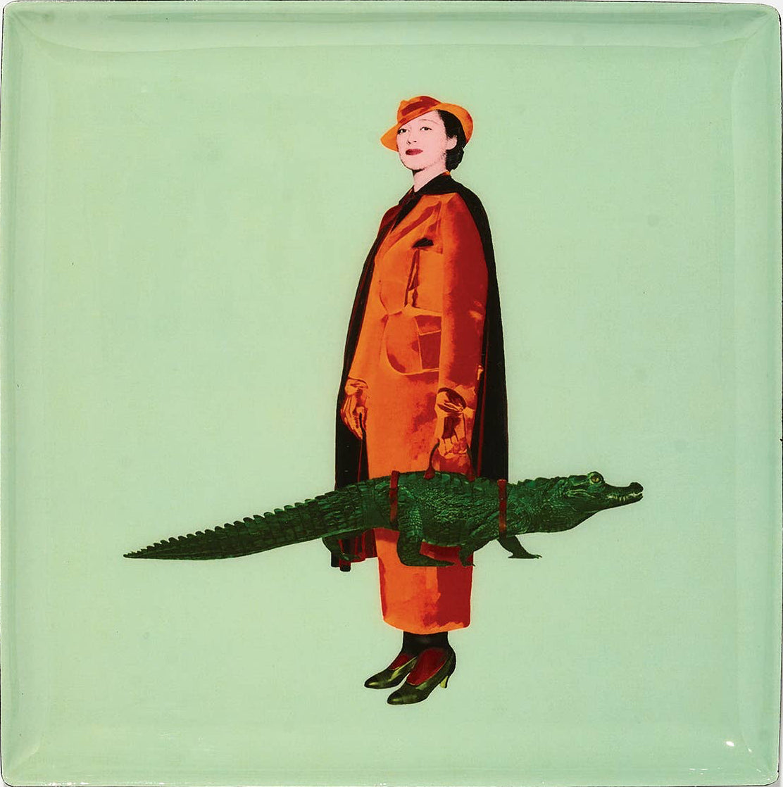 Glass coaster with a design of a woman in an orange coat and hat standing next to a green alligator on a light green background.