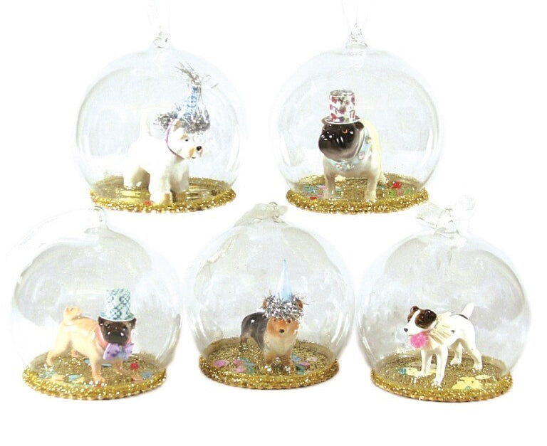 Five clear glass Christmas snow globe ornaments hanging on a white background, each containing a small dog figurine wearing a party hat and standing on a glittery gold base.