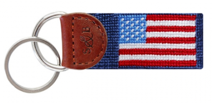 A key fob with an American flag design, featuring a leather-wrapped handle and a blue fabric strap.