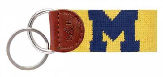 A key fob featuring the text 'MICHIGAN' and a blue and yellow needlepoint design, topped with a brown leather piece.