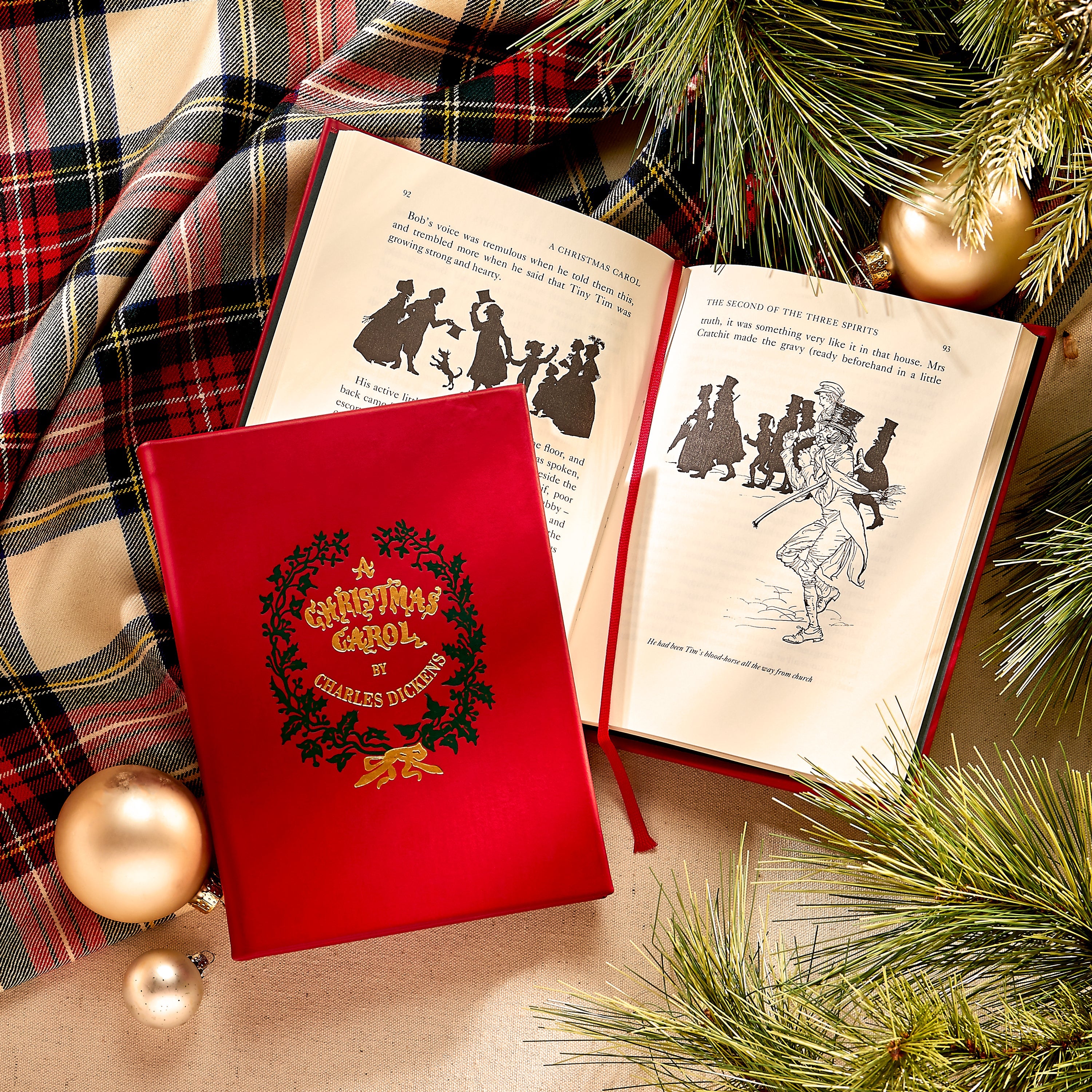 Red book cover of 'A Christmas Carol' by Charles Dickens with open book displaying illustrations, surrounded by Christmas decorations.