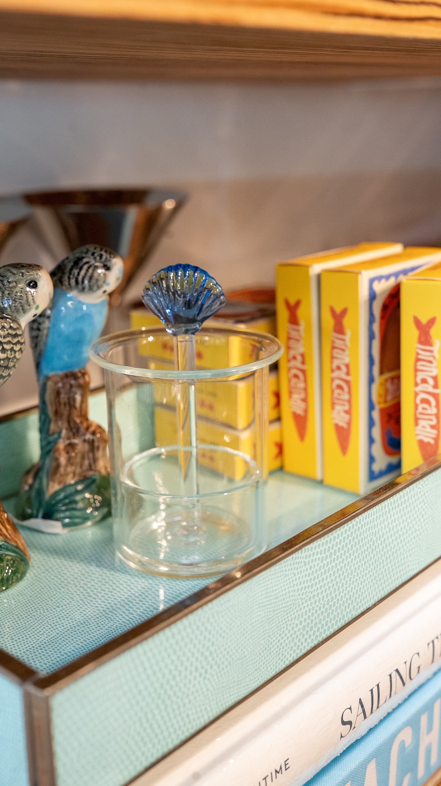 Clear glass with a blue stirrer on a shelf with books and decorative items.