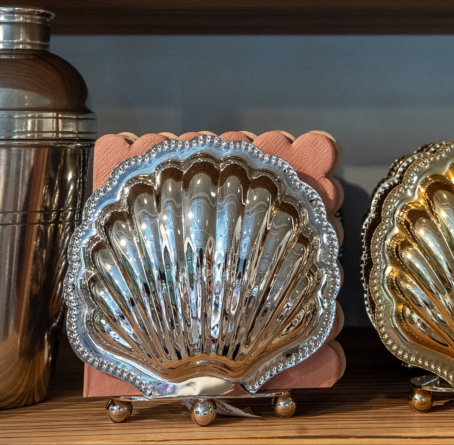 Decorative shell-shaped containers on a shelf with books and a small painting in the background.