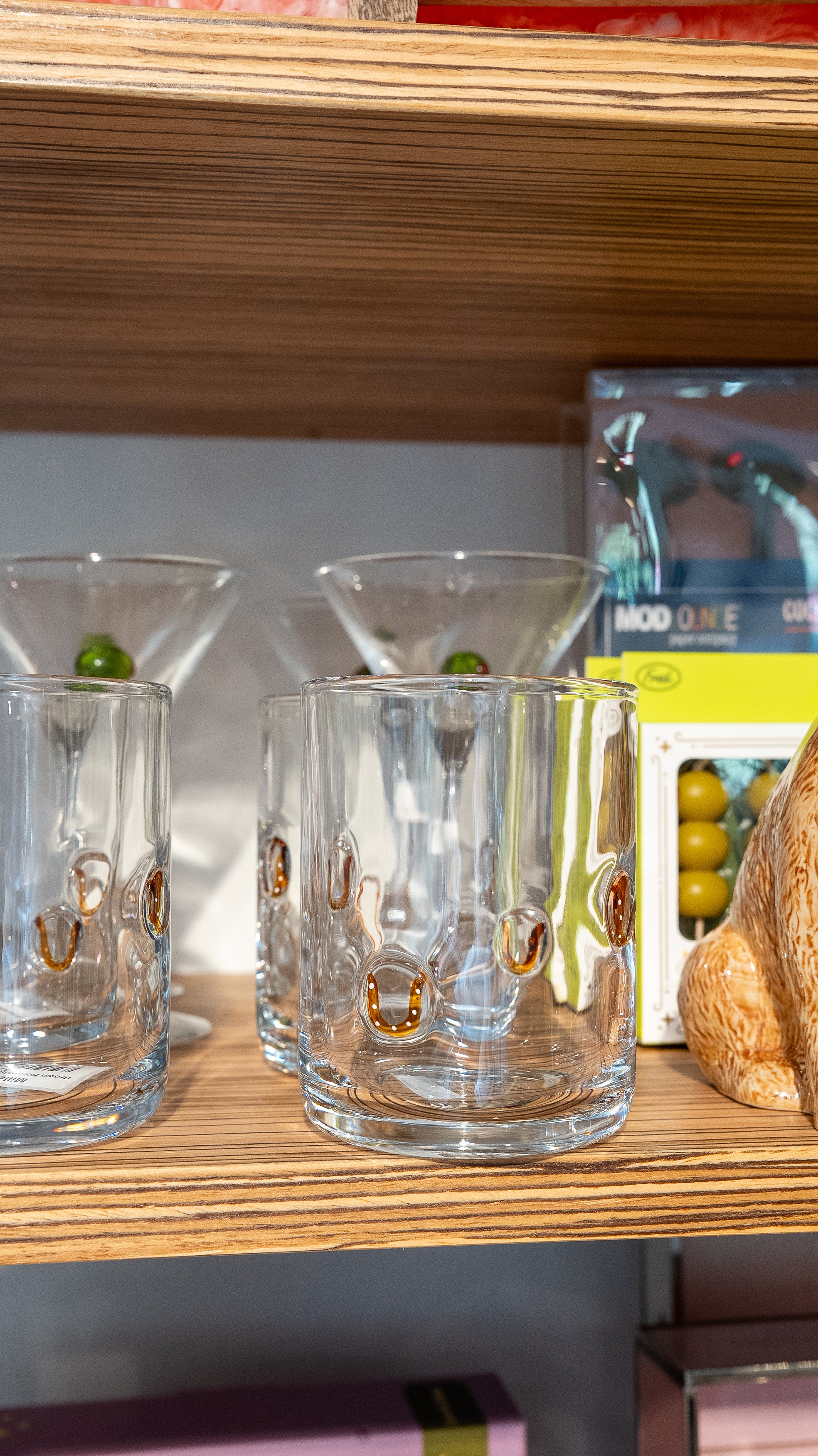 Clear glass tumblers with 'Cocktail' text on a wooden shelf.