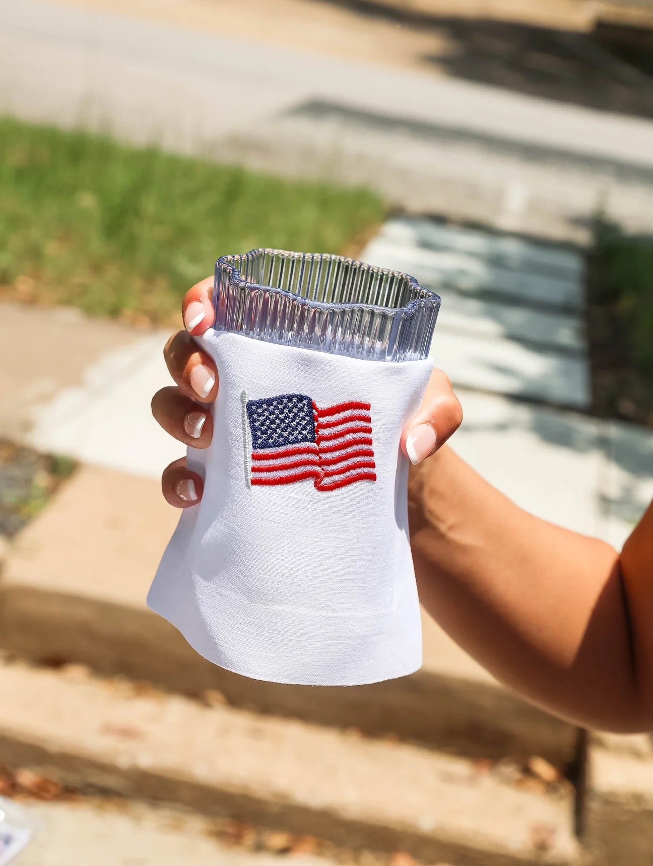Hand holding a clear plastic cup with an American flag design on a blurred outdoor background