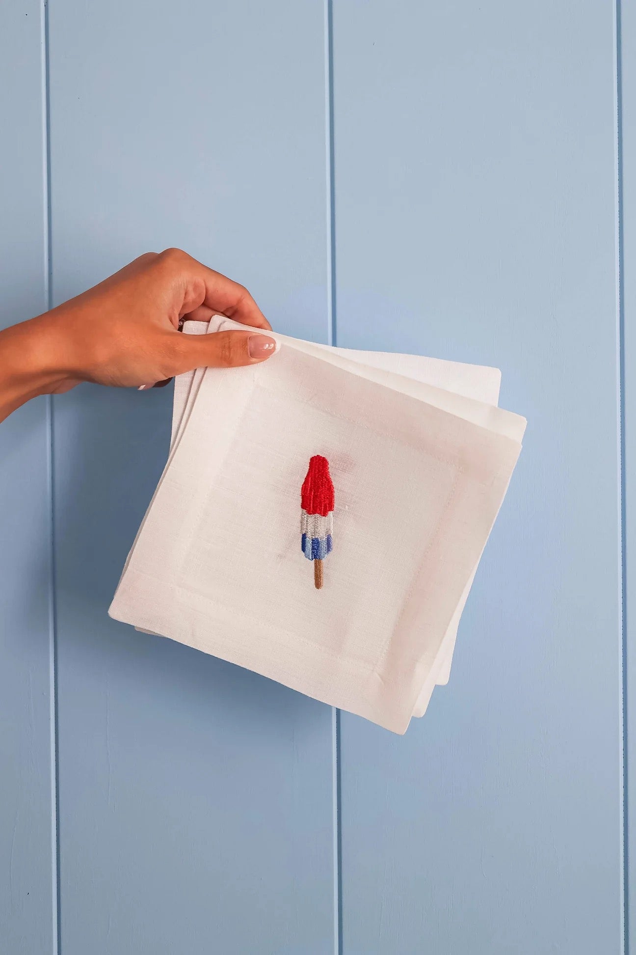 Hand holding a white napkin with a small red and blue object on a light blue background