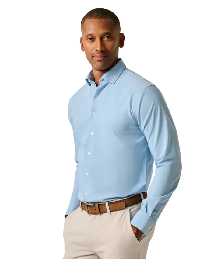 Man wearing a light blue dress shirt and beige pants against a plain background