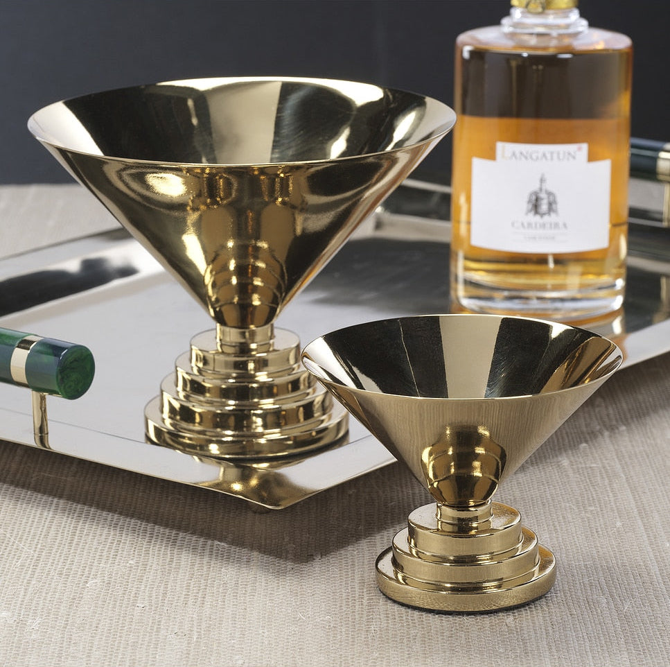 Two gold cocktail shakers on a reflective surface with a bottle of Cognac in the background.