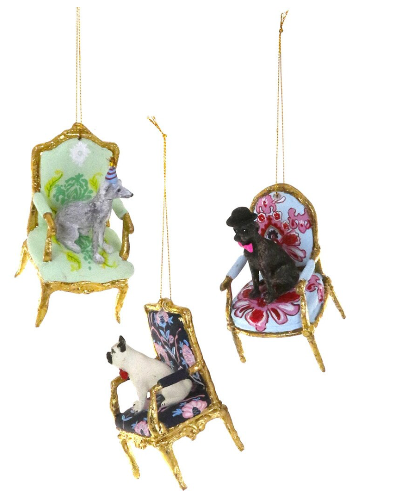 Three Christmas ornaments shaped like small vintage chairs with gold frames, each holding a different dog figurine, shown on a plain white background.