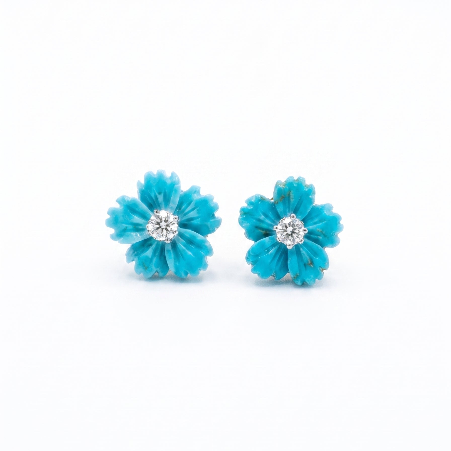 A pair of turquoise flower-shaped stud earrings with a clear round-cut gemstone in the center, set against a plain white background.