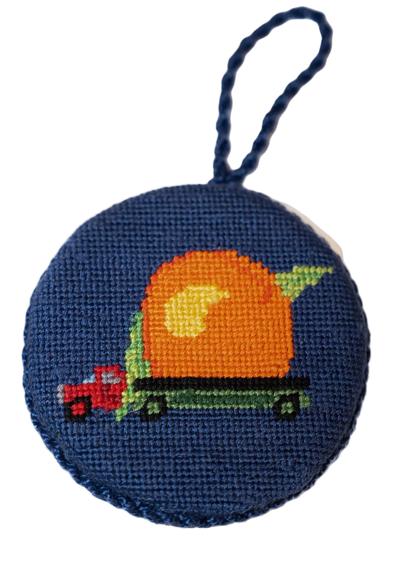 A hand-stitched needlepoint ornament featuring a blue background, a pixel-art style truck and peach, and braided rope cord detail.
