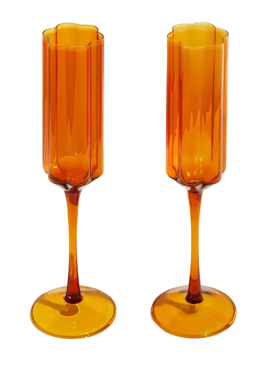 Two amber-colored champagne flutes on a white surface with a light gray background