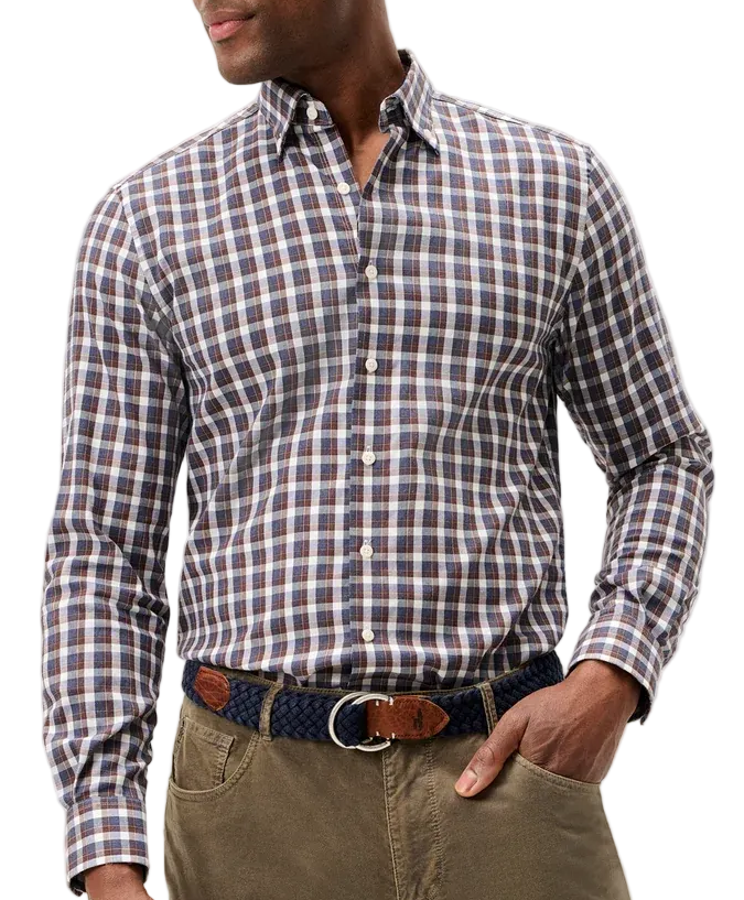 A man wearing a long-sleeve button-down shirt with a brown, white, and blue checkered pattern, paired with olive green trousers and a patterned belt, photographed against a light gray studio background.