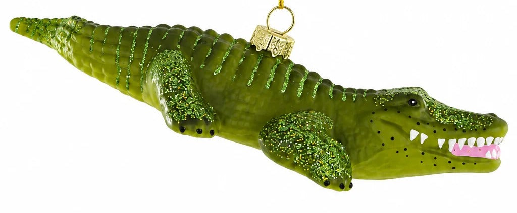 A green glittery crocodile ornament with an open mouth showing white teeth, suspended by a gold string against a plain white background.