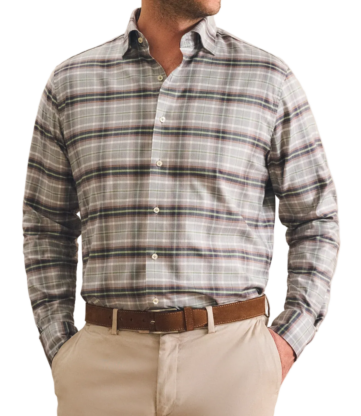 A man wearing a long-sleeve plaid button-down shirt in gray, white, and brown, paired with beige trousers and a brown belt, standing against a textured beige wall.