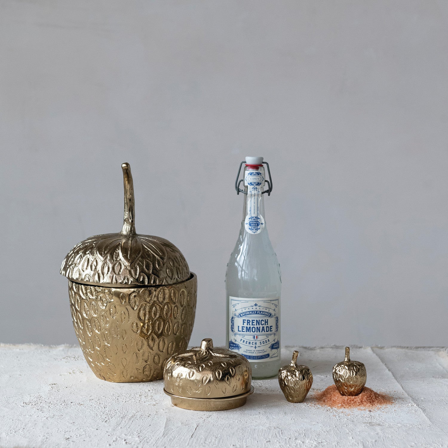 Gold decorative items and a bottle of French Lemonade on a light surface with a gray background