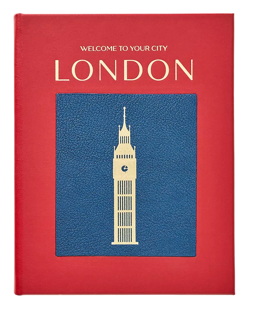 A red hardcover book or travel guide featuring 'WELCOME TO YOUR CITY LONDON' in gold lettering and a blue textured square with a cream-colored Big Ben illustration on the front, photographed against a light beige background.