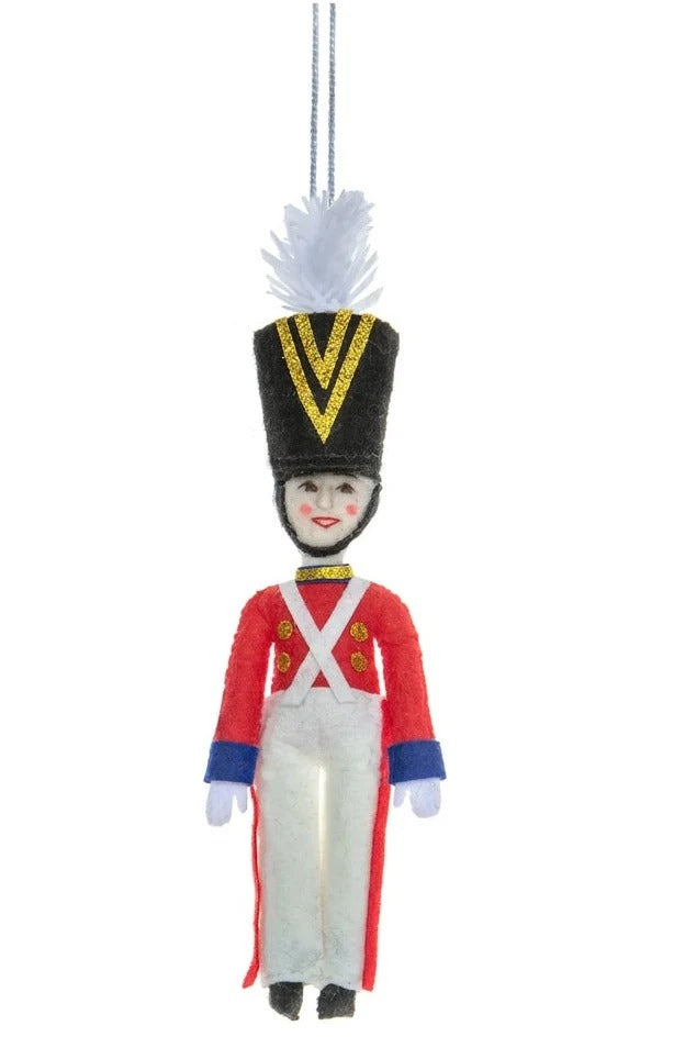 Decorative Christmas ornament of a toy soldier in red uniform with white pants on a white background