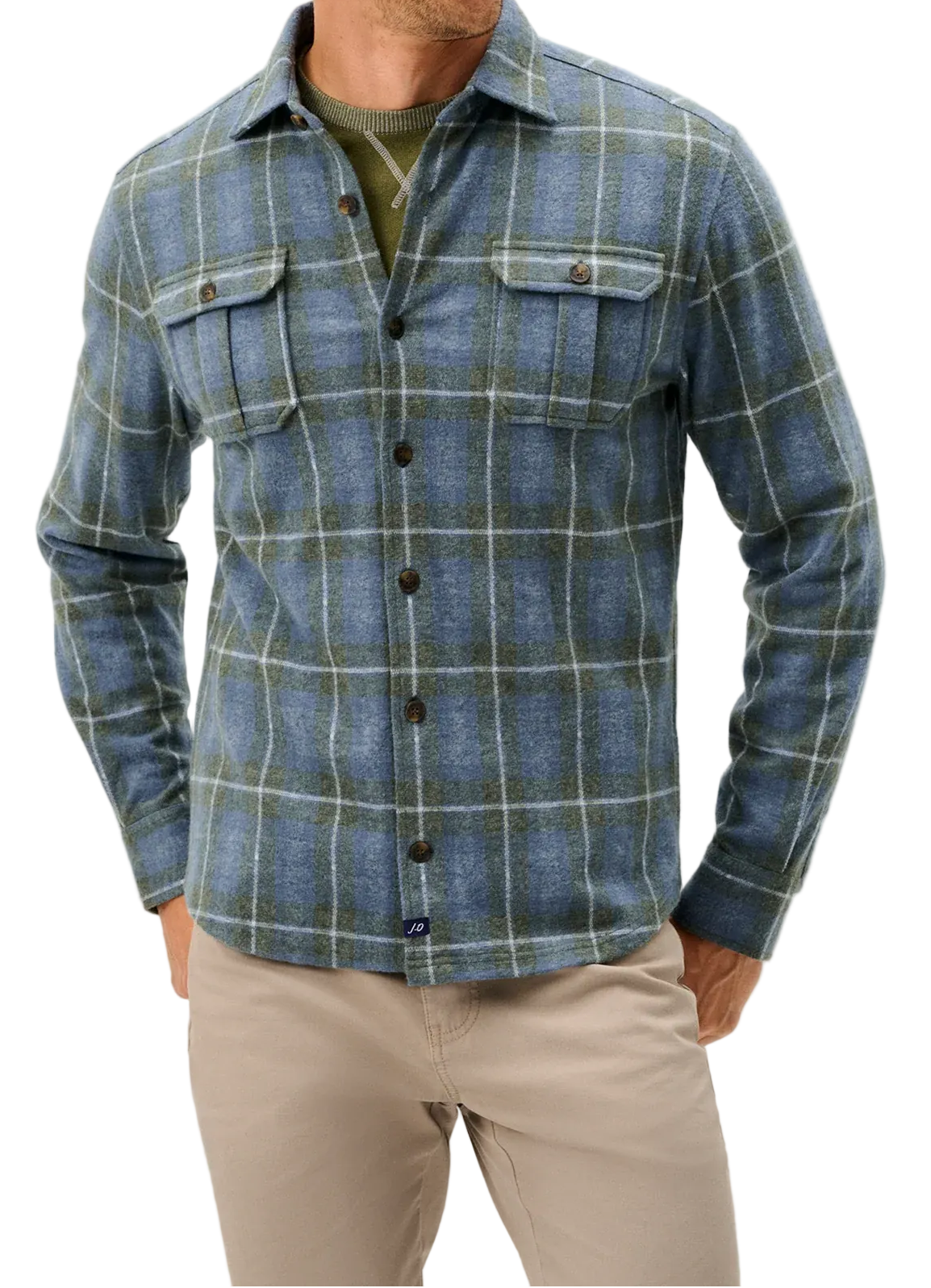 A man wearing a blue and green plaid button-down flannel shirt over an olive green undershirt, paired with beige pants, against a light gray studio background.