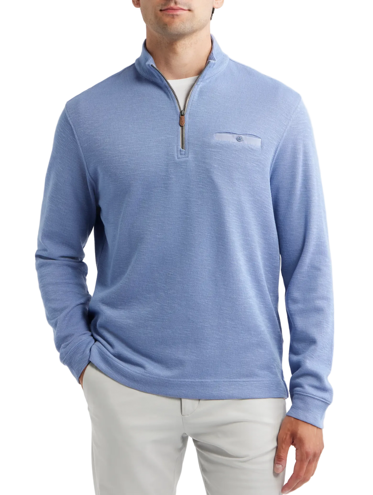 A man wearing a light blue quarter-zip knit sweater with a chest pocket, paired with light gray trousers, against a plain light gray background.