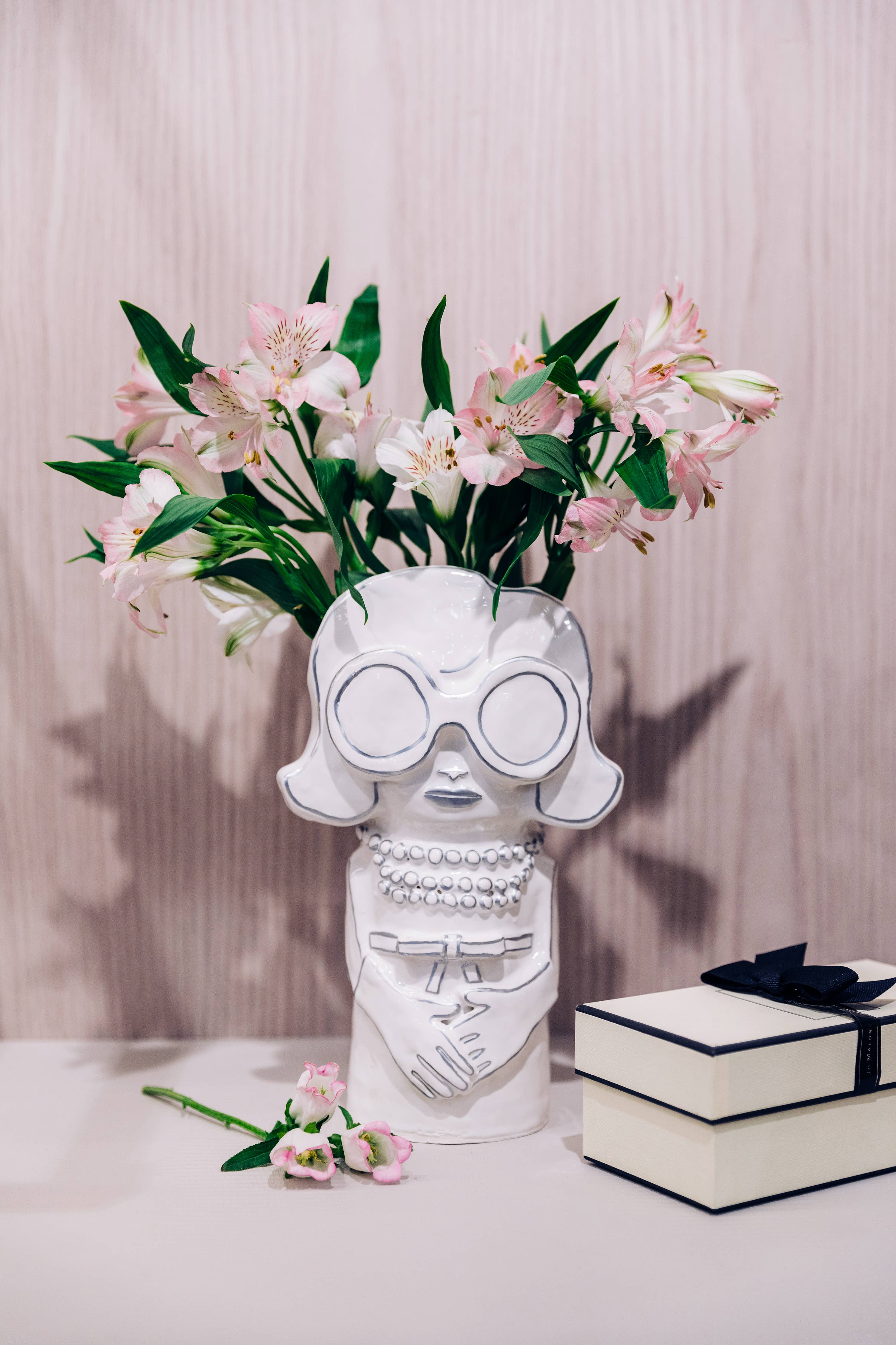 White ceramic vase shaped like a face with glasses holding flowers on a table.