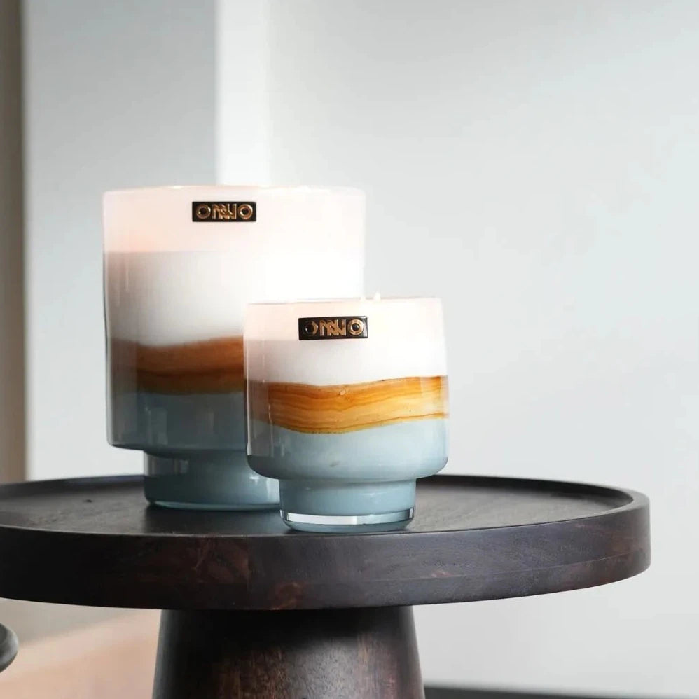Two candles with gradient design on a small round wooden table.