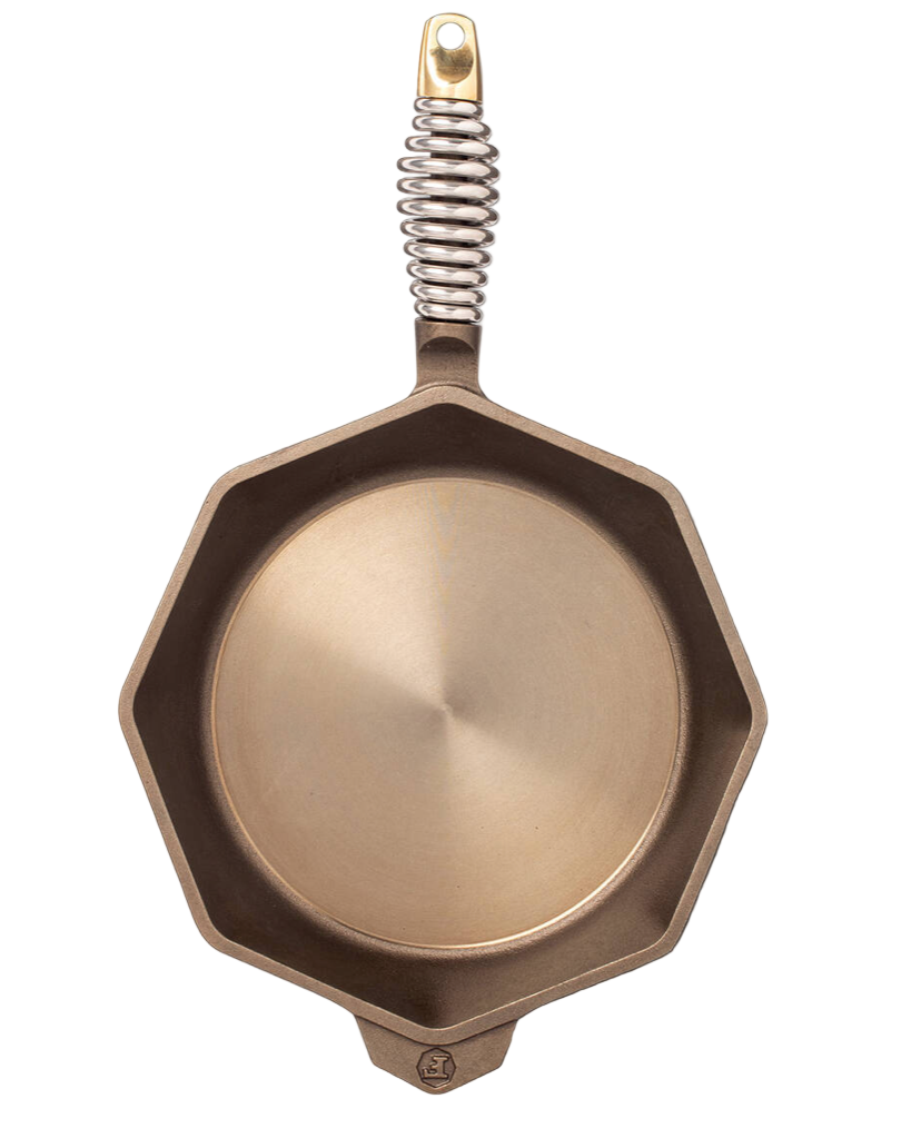 Bronze-colored cast iron frying pan with a spring on a white background