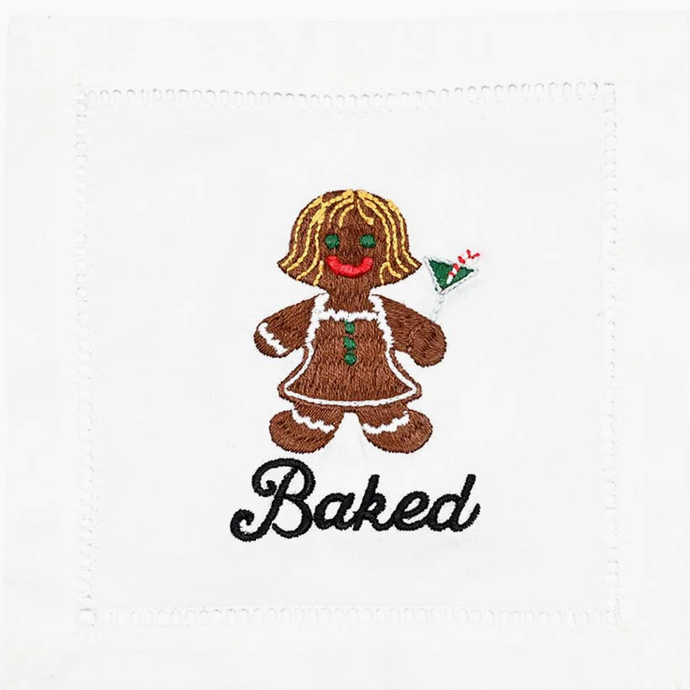 A white cocktail napkin with a text pattern featuring the word 'BAKED' and an illustration of a smiling gingerbread character holding a green umbrella, cocktail umbrella, and a green tag.