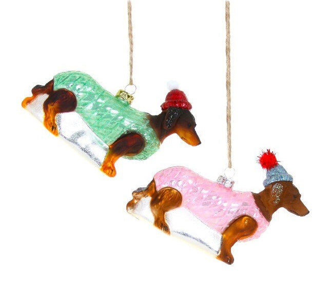 Two glass dog ornaments wearing colorful sweaters hanging on a white background