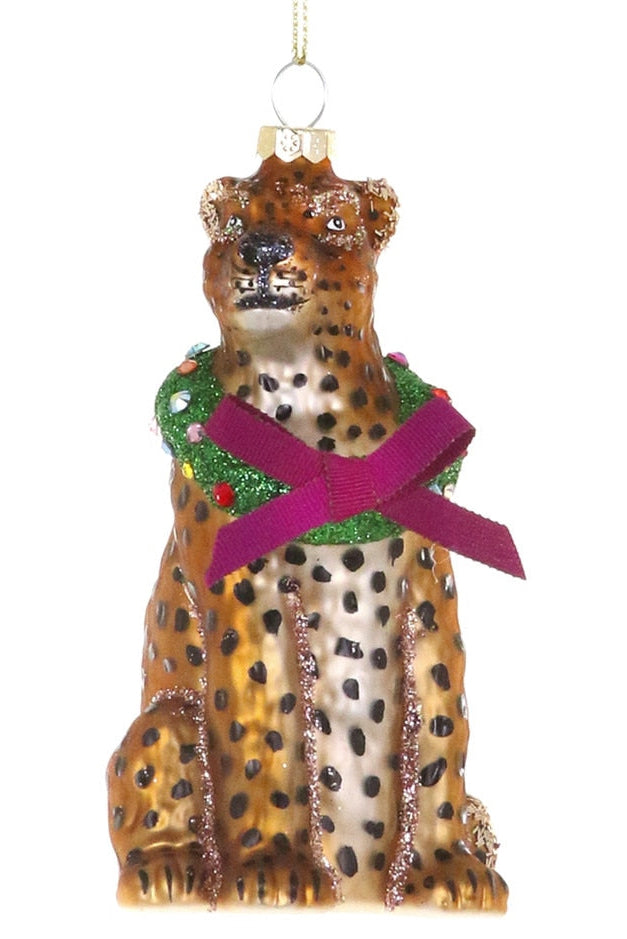 Decorative glass ornament of a cheetah with a purple bow and greenery on a white background