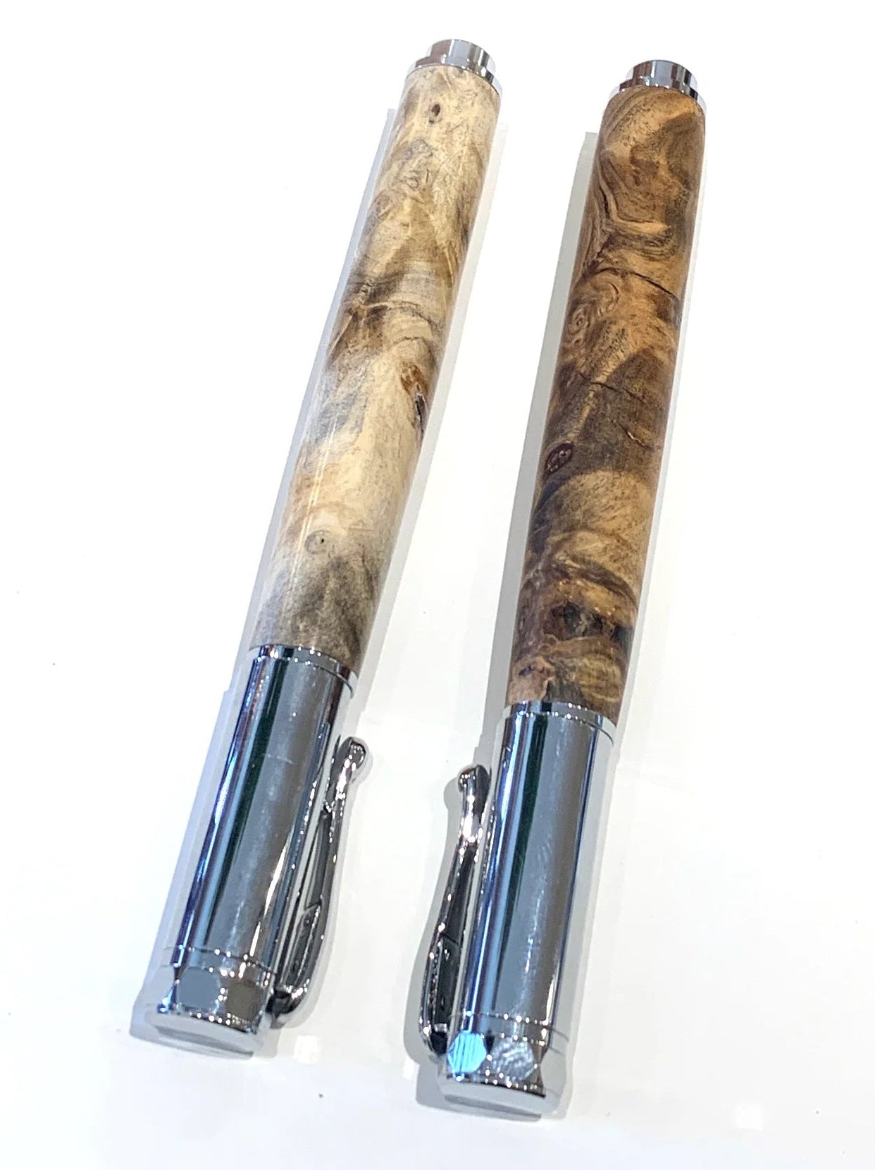 Two slim metal pens with marbled wood-grain barrels, one in light tan and the other in dark brown, displayed on a clean white background.