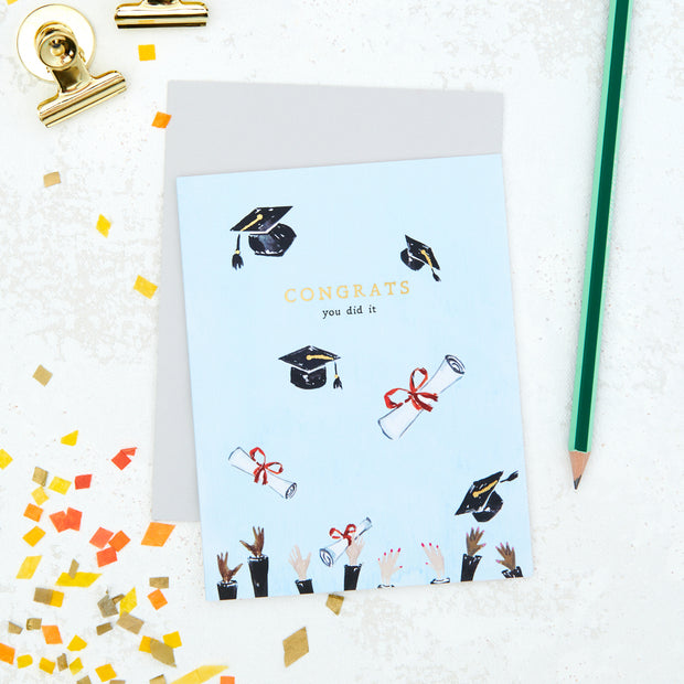Graduation-themed card with illustrations and 'Congrats you did it' text on a light blue background, surrounded by confetti and a pencil.