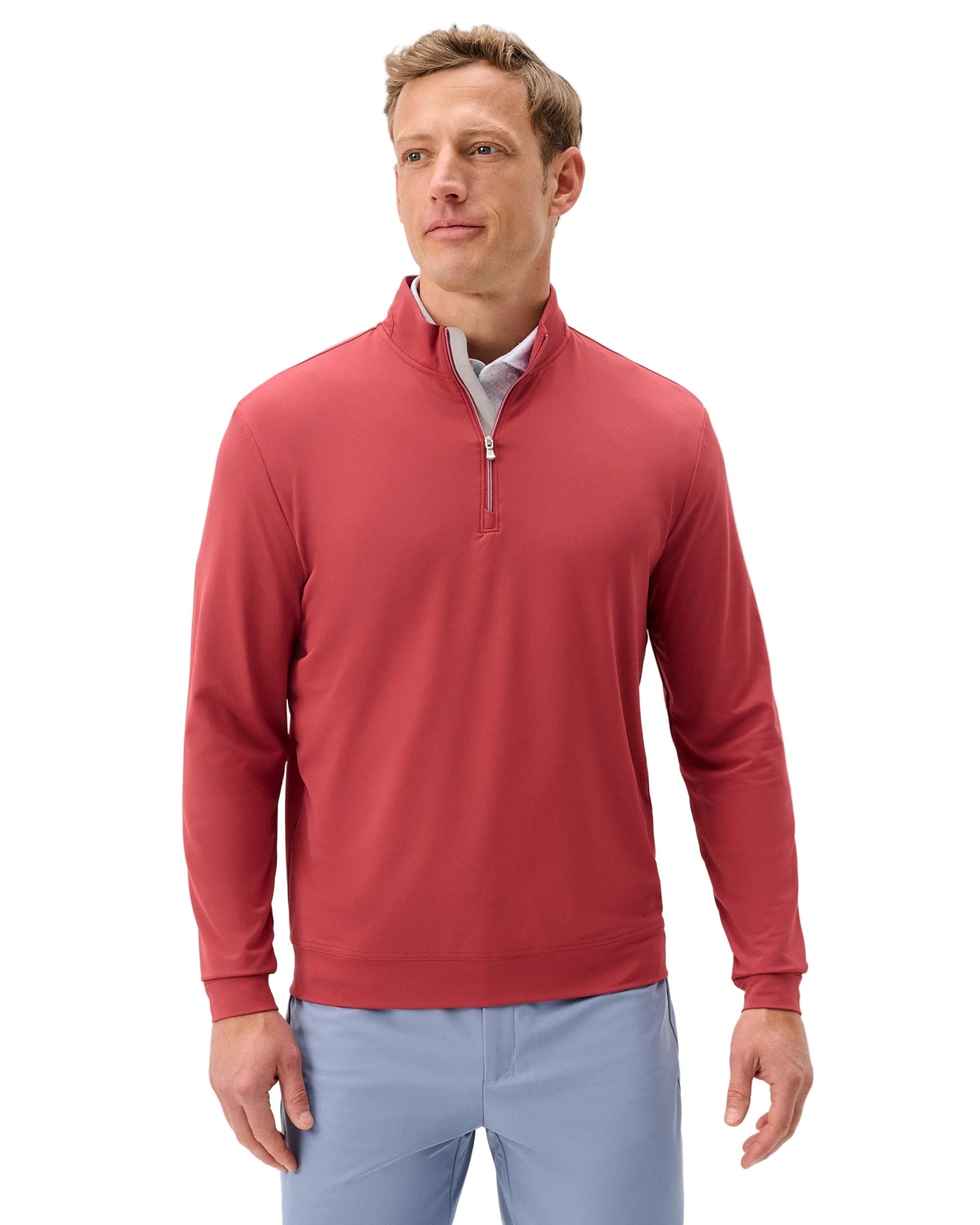 Man wearing a red quarter-zip pullover and light blue pants on a white background