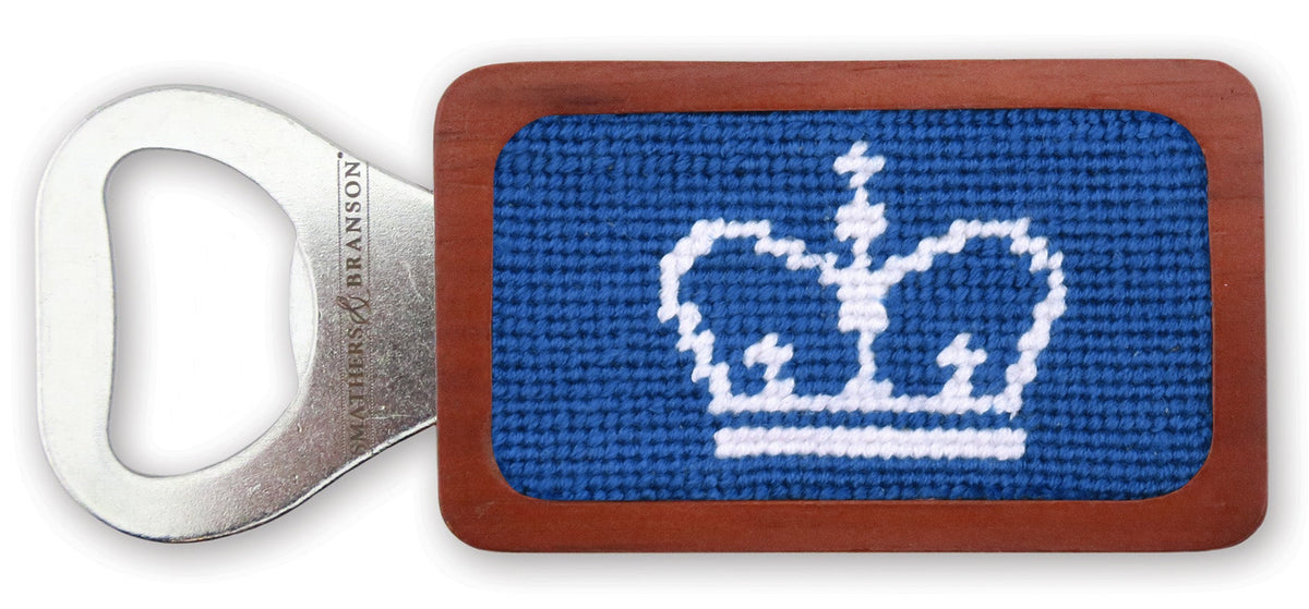 A rectangular metal bottle opener with a blue and white embroidered crown design on the front, set against a plain white background.