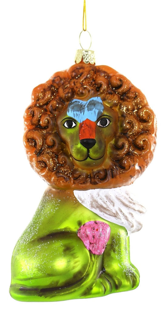 A hand-painted glass Christmas ornament shaped like a lion with a curly brown mane, green body, blue and red face details, and a pink flower on its back, shown against a plain white background.