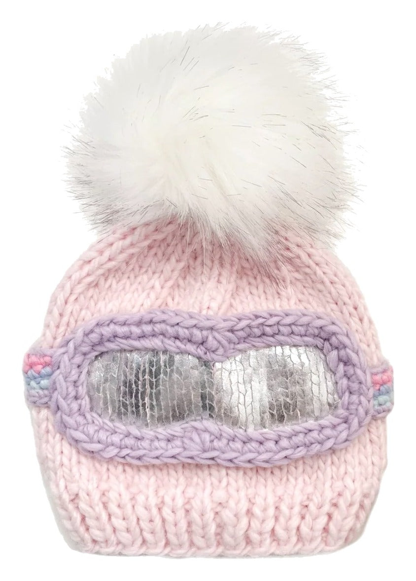 Pink knit beanie with goggles and white fur pom-pom on a light gray background