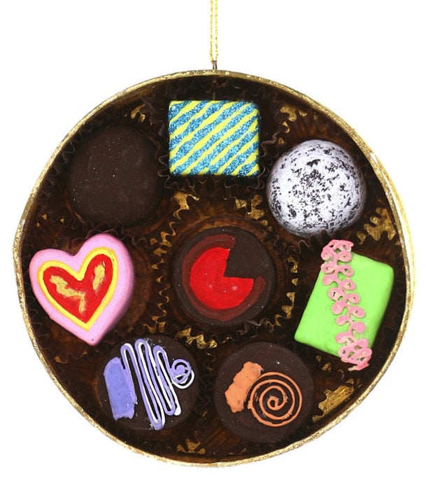 A round chocolate-themed ornament or tray filled with assorted candy and chocolate pieces, hanging from a thin gold string against a plain white background.