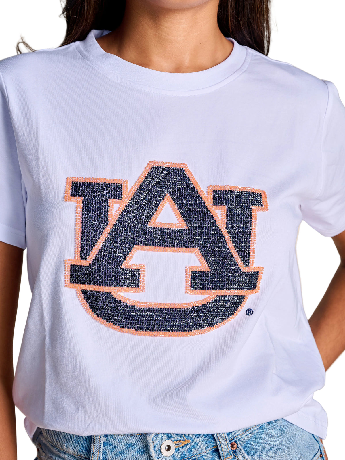 A close-up of a person wearing a white short-sleeve T-shirt with a large navy and orange 'AU' auburn logo across the chest, paired with light blue jeans against a plain beige background.