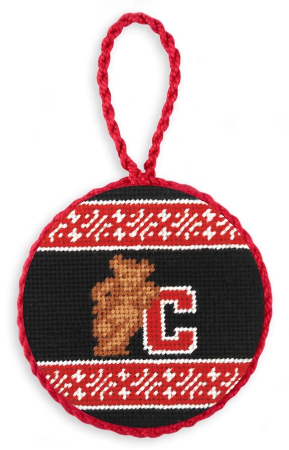 A round cross-stitch ornament featuring a black center with a brown bear head and a red-and-white letter C, surrounded by red and white knit-style borders, with a red hanging loop at the top.