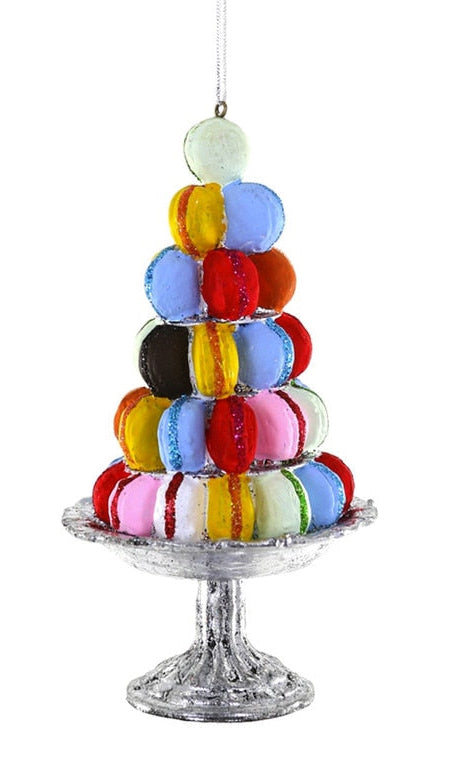 A colorful macaron tower decoration shaped like a Christmas tree, displayed on a silver pedestal stand against a plain white background.