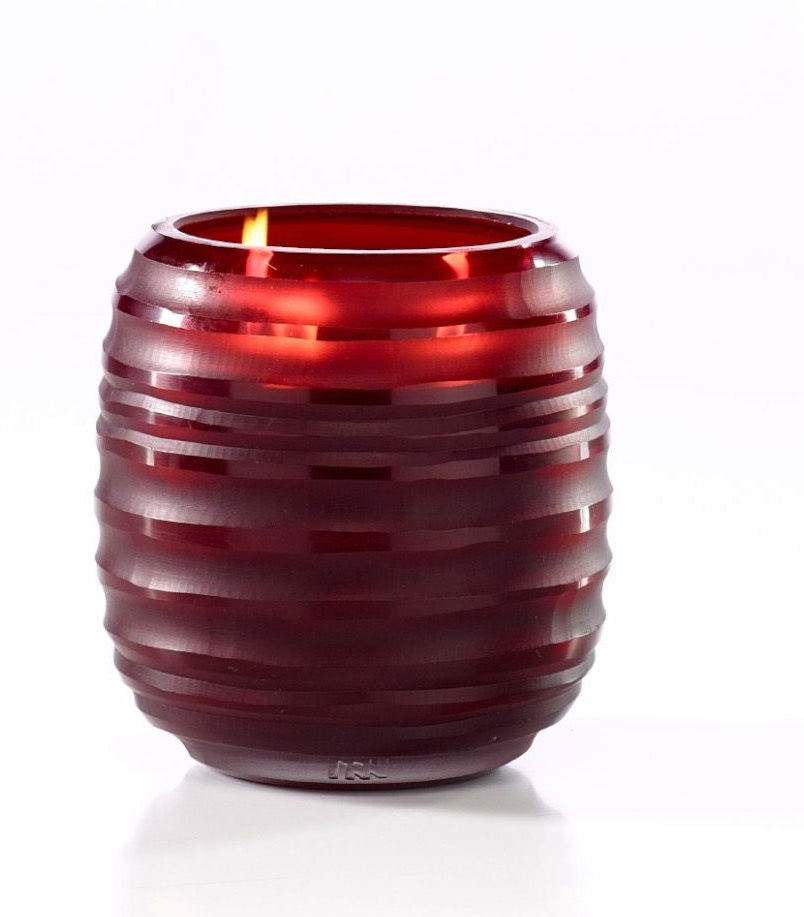 A lit red ribbed glass candle holder on a clean white background.