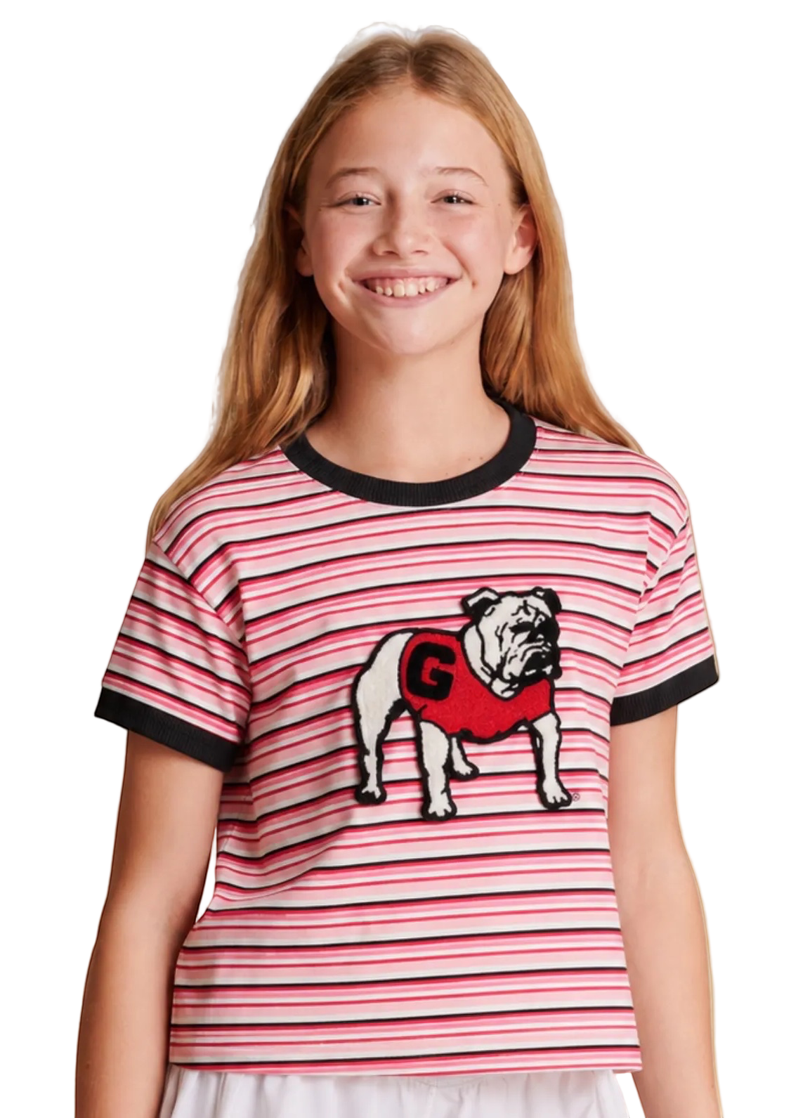 A young girl smiling while wearing a red and white striped ringer t-shirt with a bulldog graphic and white shorts, set against a solid beige studio background.