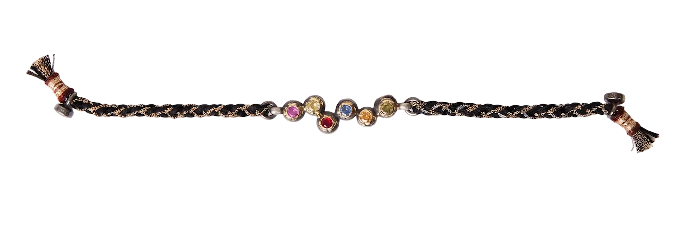 A braided dark brown cord patricia arrango bracelet with a central cluster of small round gemstones in various colors, finished with tassel ends on a white background.
