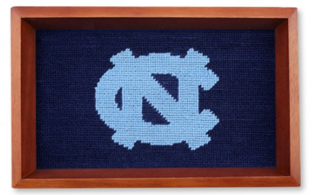 A needlepoint valet tray featuring the University of North Carolina at Chapel Hill logo, primarily in blue and white colors, framed in a brown wooden box.